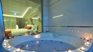 A modern bathroom with a large bathtub surrounded by candles, a mirror, and a view of a bedroom. - Ramada by Wyndham Usak (Usak)