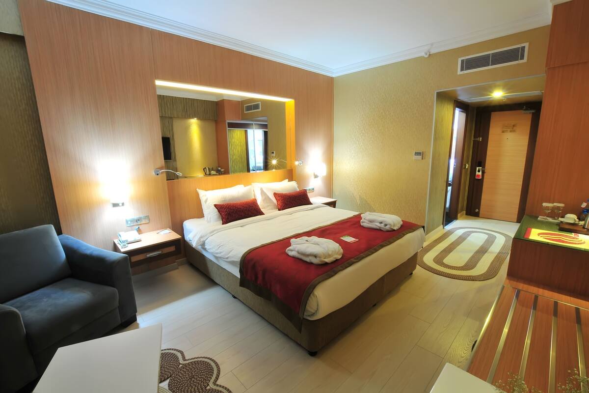 A hotel room with a large bed, a bedside table, a chair, and a desk with a computer.