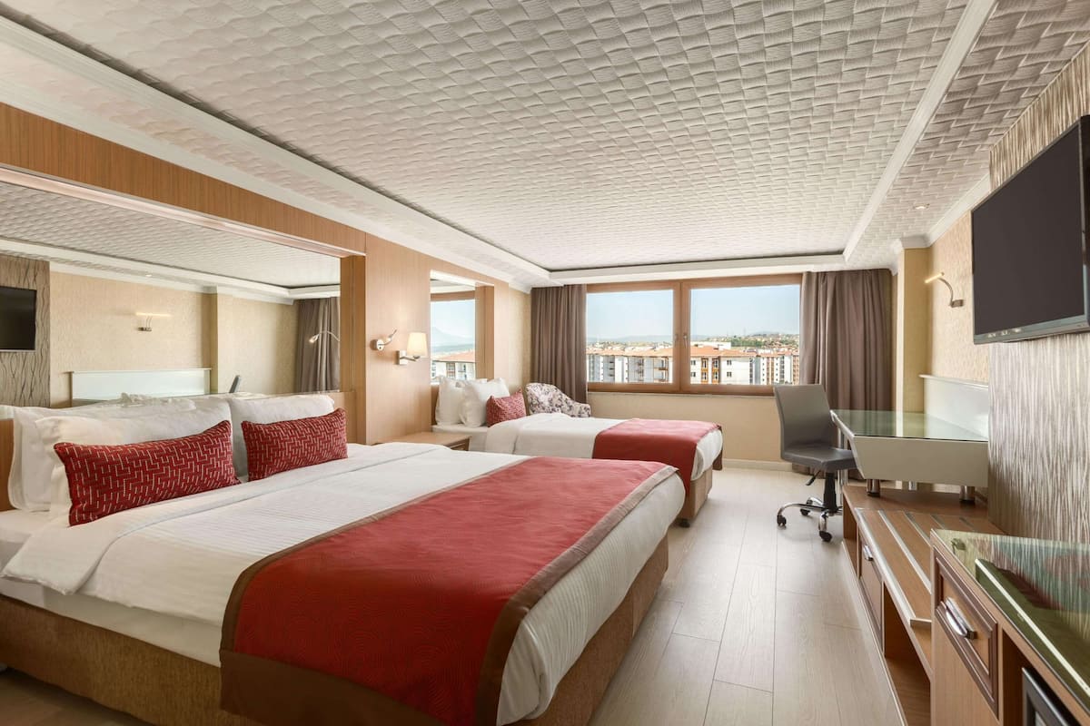 A hotel room with two beds, a desk, a chair, and a TV.