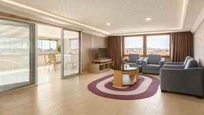 A modern living room with a flat-screen TV, grey sofas, a coffee table, and a large window with a city view. - Ramada by Wyndham Usak (Usak)