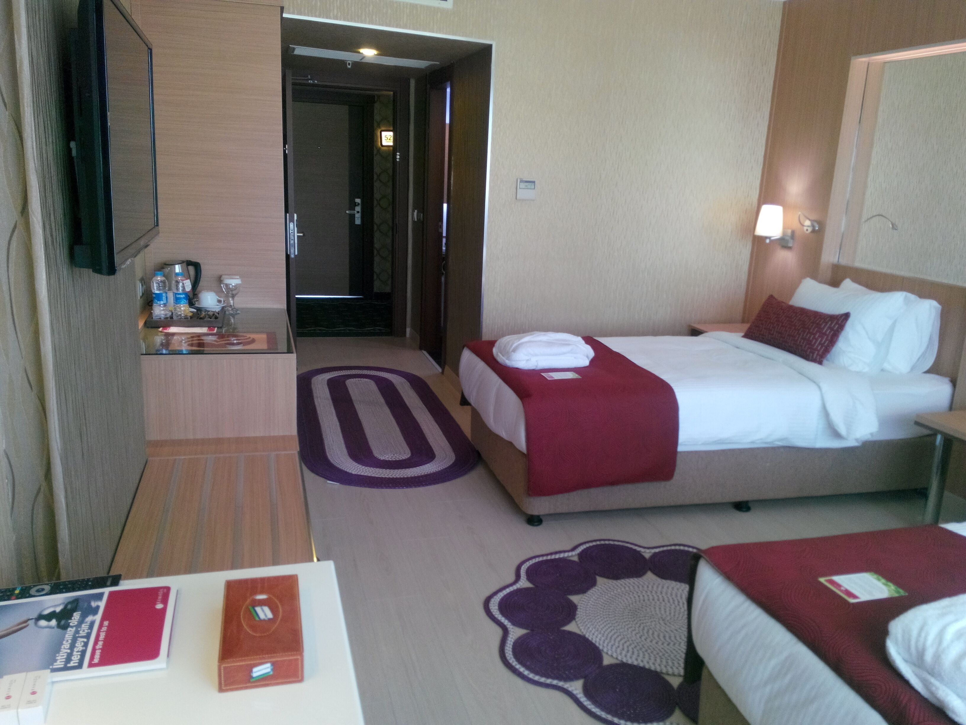 Habitación de hotel con dos camas, un escritorio, un televisor y un baño visible a través de una puerta abierta.