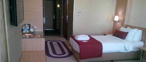 Habitación de hotel con dos camas, un escritorio, un televisor y un baño visible a través de una puerta abierta.