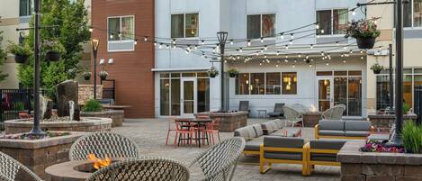 An outdoor patio area with wicker chairs, a fire pit, and string lights.