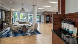 A modern lobby with a stone accent wall, a seating area with a round table and chairs, and a coffee station with dispensers.