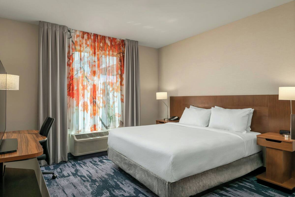 Een hotelkamer met een groot bed, een bureau met stoel, een lamp en een raam met gordijnen.