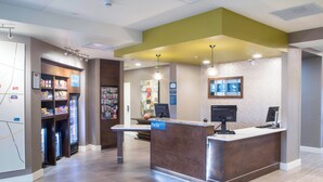 A reception area with a reception desk, a vending machine, and a wall-mounted information board. - TownePlace Suites Oxford (Oxford)