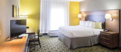 A hotel room with a bed, bedside tables, a desk with a TV, and a patterned carpet.
