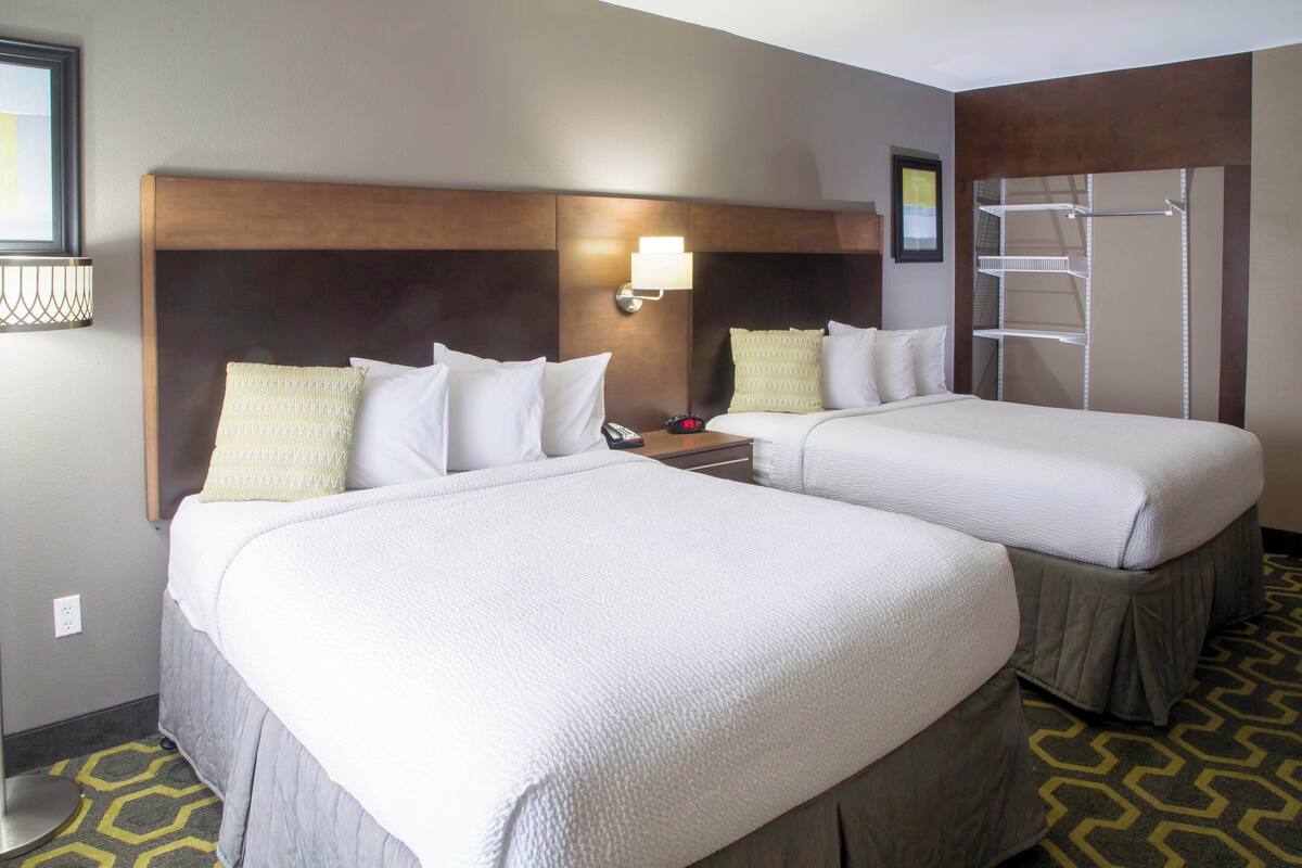 Habitación de hotel con dos camas, una mesita de noche, una lámpara y un armario empotrado.