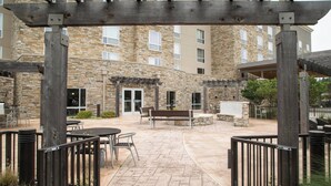 An outdoor patio area with stone flooring, wooden benches, and tables. - TownePlace Suites Oxford (Oxford)