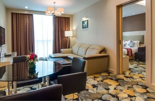 Habitación de hotel con sofá, una mesa de comedor con sillas, lámpara y cama con cabecera.