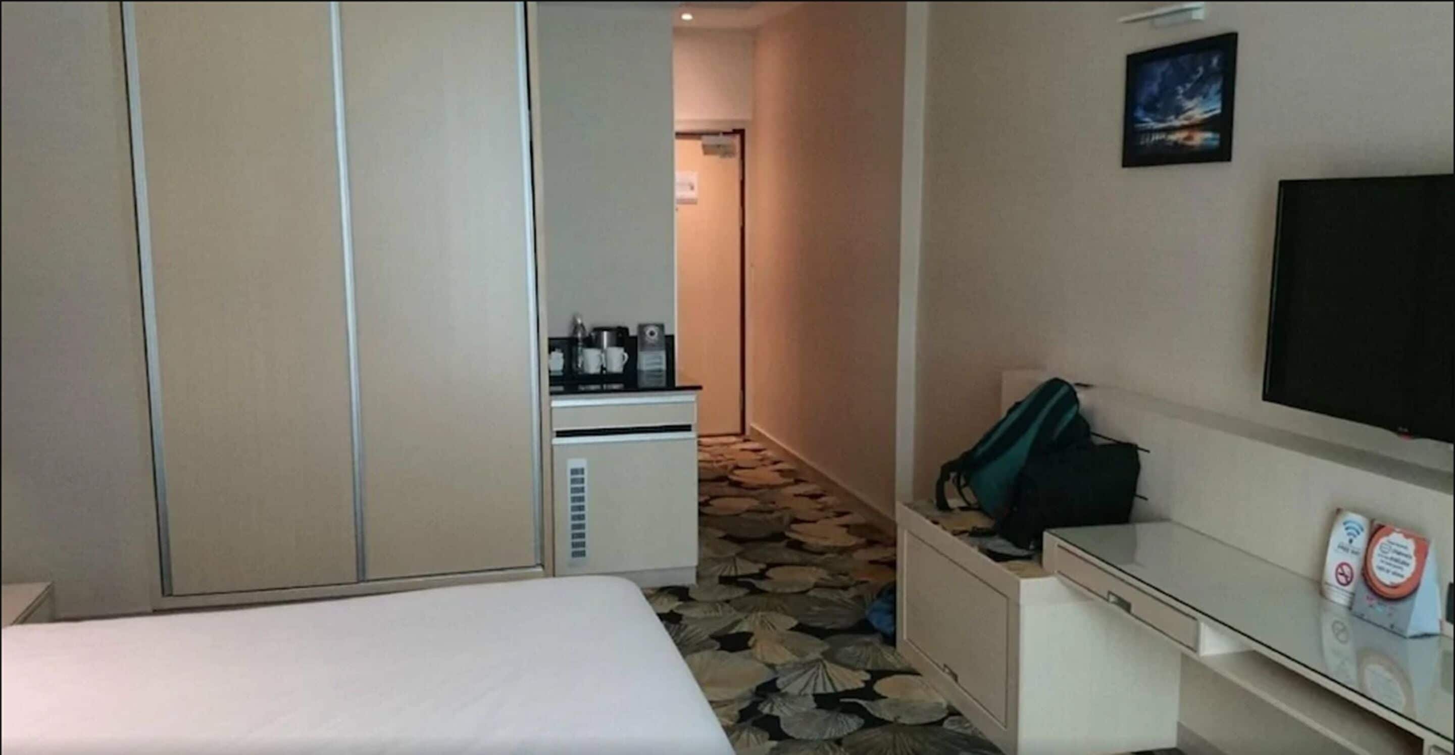 A hotel room with a bed, a desk with a computer, a TV, and a kitchenette with a coffee maker.