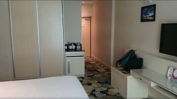 A hotel room with a bed, a desk with a computer, a TV, and a kitchenette with a coffee maker.