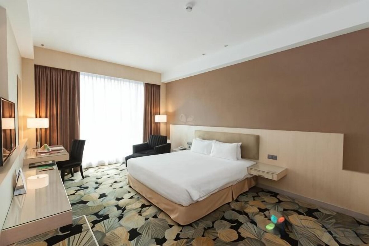 Una habitación de hotel con una cama grande, un escritorio con una silla, un televisor y una ventana con cortinas.