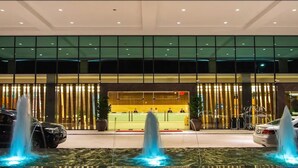Un hall d’hôtel moderne comprenant un comptoir d’accueil, un espace salon et un élément décoratif aquatique avec des fontaines.