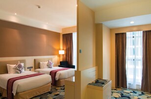Habitación de hotel con dos camas, un escritorio, una silla y un gran ventanal con cortinas.