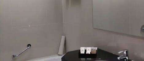 A modern bathroom with a black countertop, white sink, and a large mirror. There is a towel rack with a folded towel and a toilet paper holder.