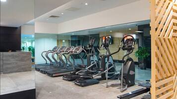 A gym with multiple treadmills and ellipticals, a reception desk, and a glass wall reflecting the interior.