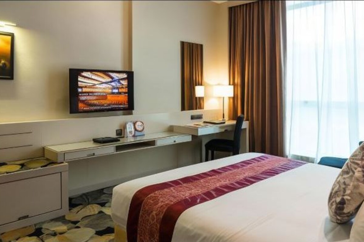 A hotel room with a bed, a desk, a chair, a television, and a window with curtains.