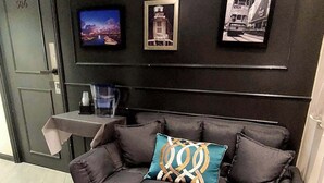 A modern living room with a dark grey sofa, a teal and gold throw pillow, and a small table with a water bottle and cups. - 9 Boutique Hotel (Hong Kong)