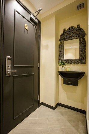 A dark wooden door with a keypad lock and a small keyhole, a wall-mounted mirror with an ornate frame, and a black vanity with a sink and a plant. - 9 Boutique Hotel (Hong Kong)