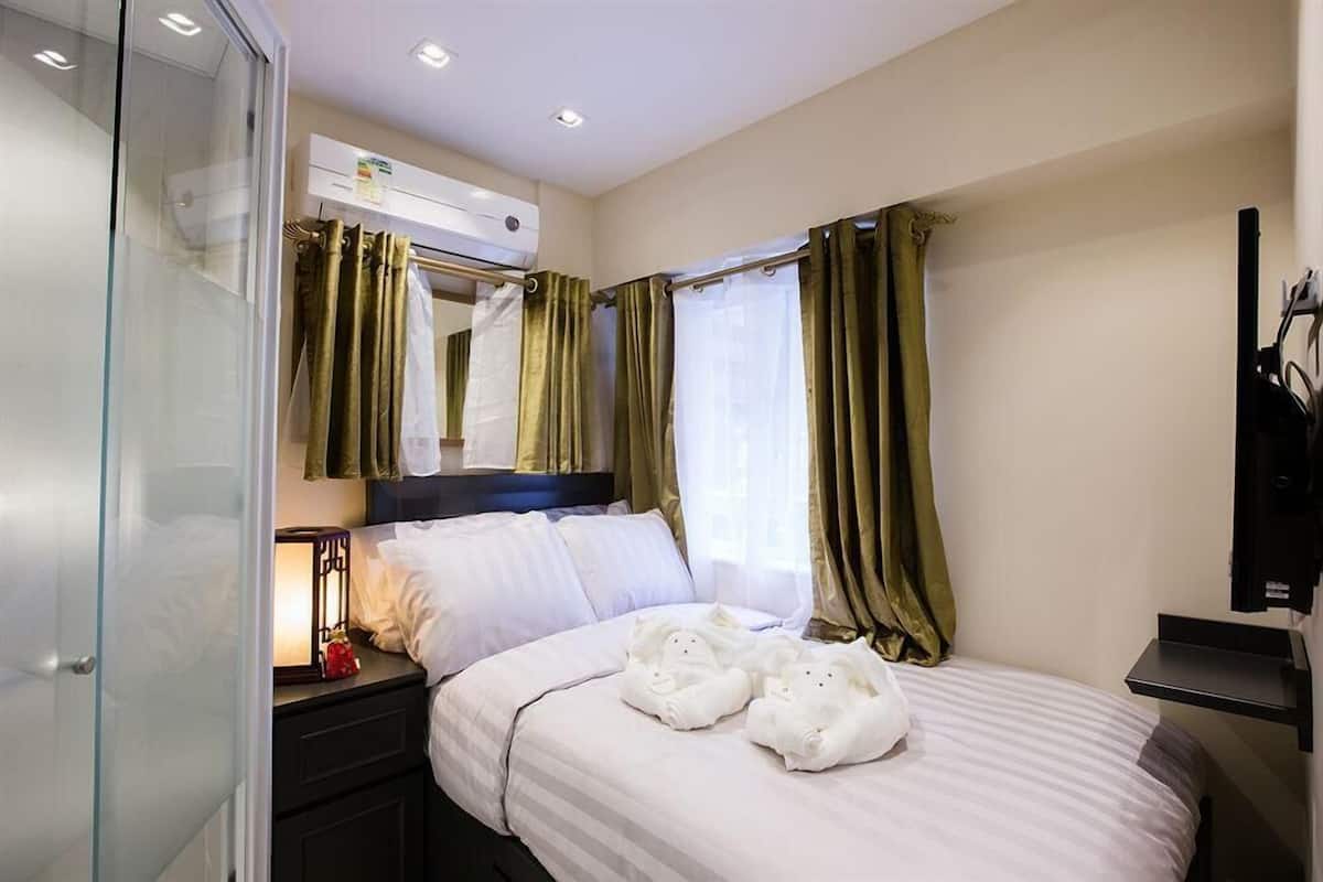 A hotel room with a bed, a bedside table with a lamp, a mirror, and a window with curtains.