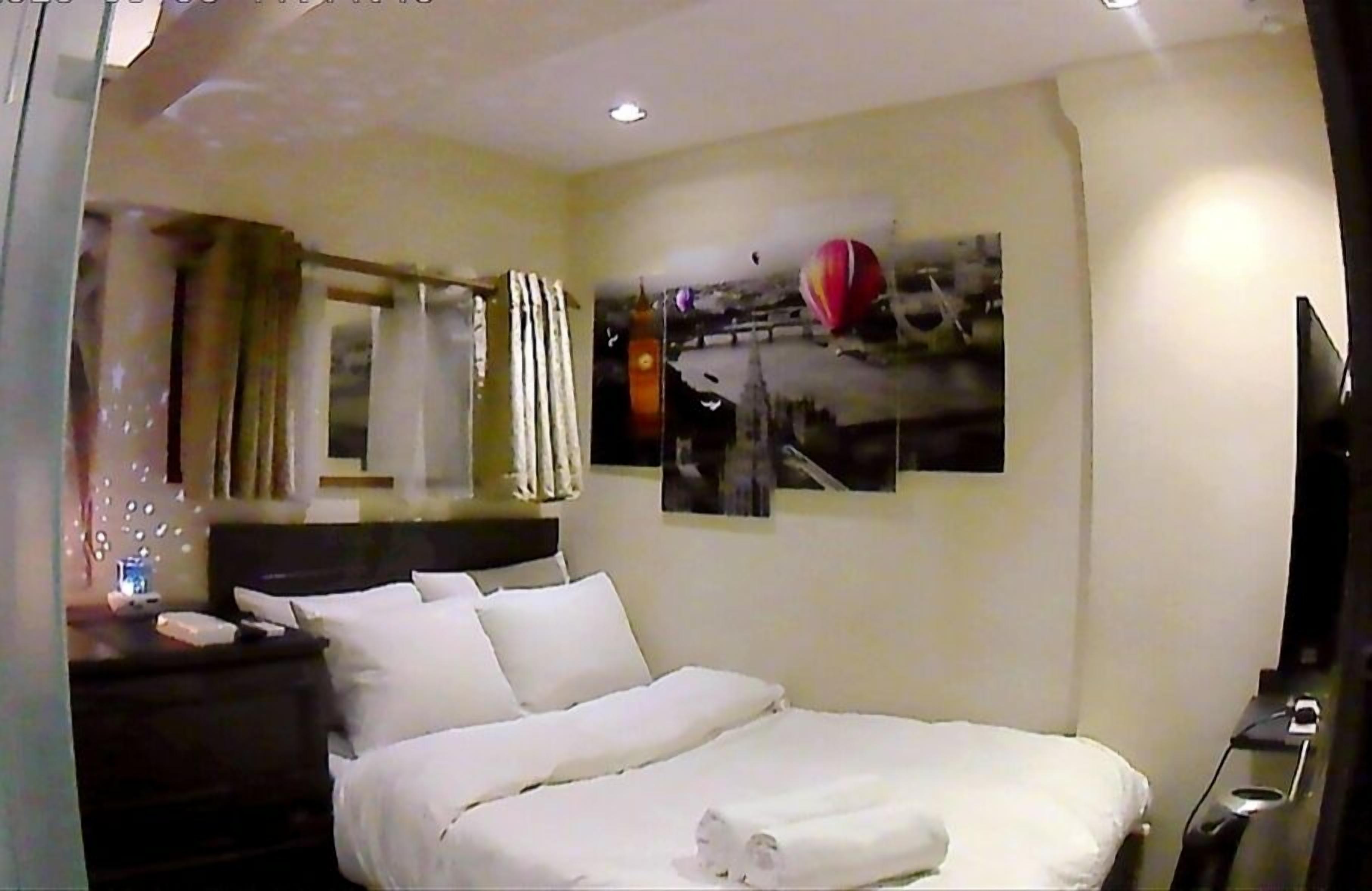 A hotel room with a bed, a nightstand, a mirror, and a wall-mounted TV.
