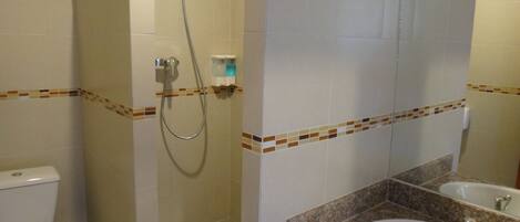 Un baño con inodoro, ducha con cabezal de ducha manual y lavabo con espejo superior.