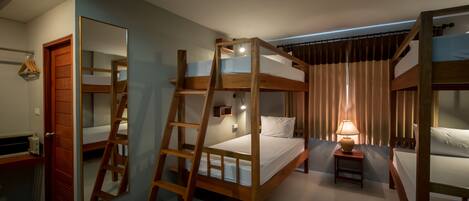 A bunk bed room with a ladder, a small table with a lamp, and a mirror on the wall.