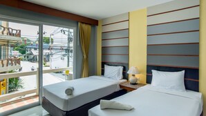 Una habitación de hotel con dos camas, una ventana que da a la calle y una mesita de noche con una lámpara.