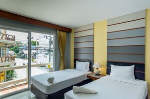 A hotel room with two beds, a window with a view of the street, and a bedside table with a lamp.