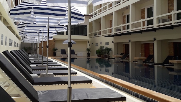 Zona de piscina con sombrillas a rayas, sillas de descanso y una piscina reflectante.