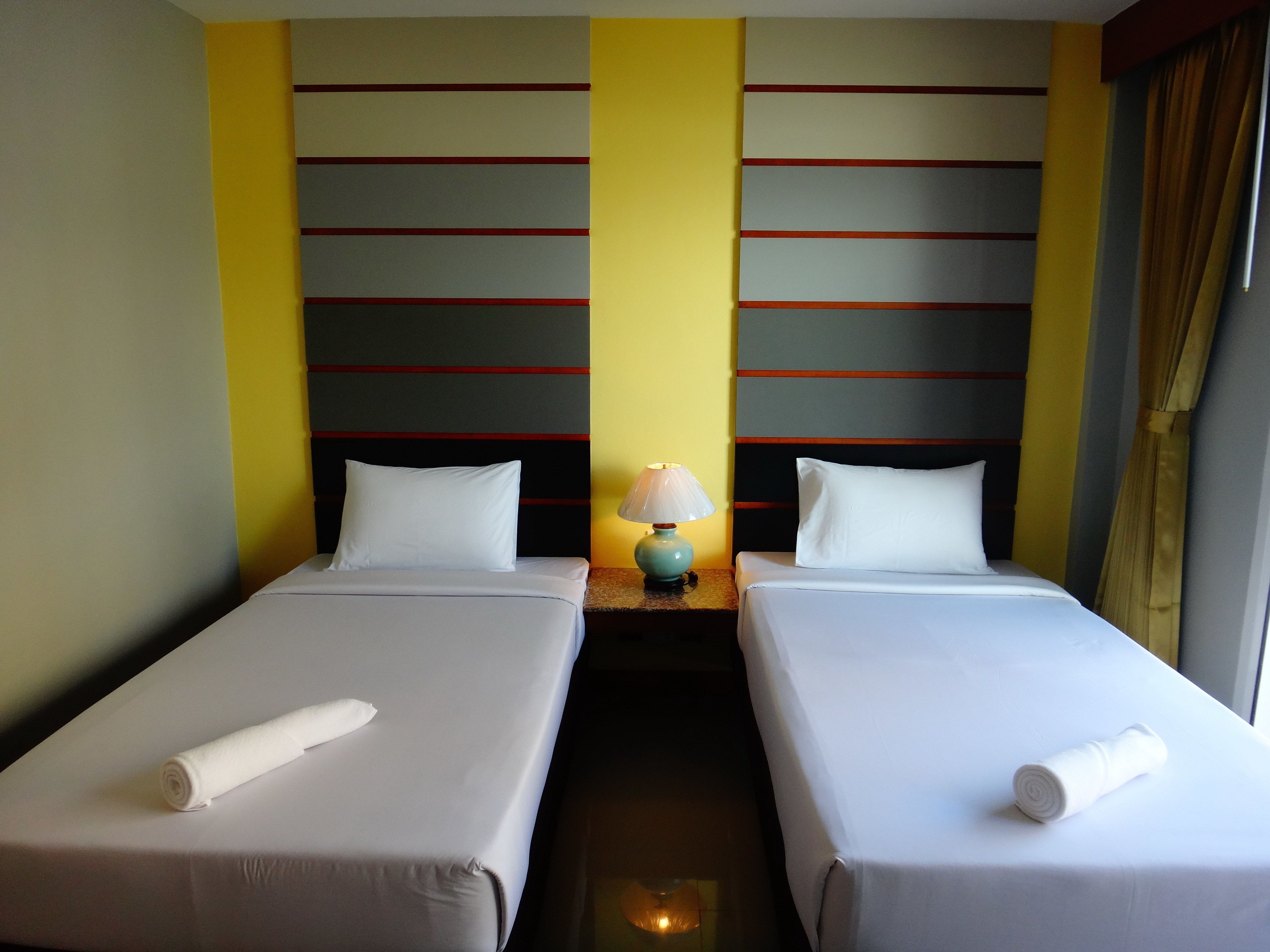 Une chambre d’hôtel avec deux lits simples, une table de chevet avec une lampe et une fenêtre avec des rideaux.