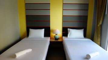 Una habitación de hotel con dos camas individuales, una mesita de noche con lámpara y una ventana con cortinas.