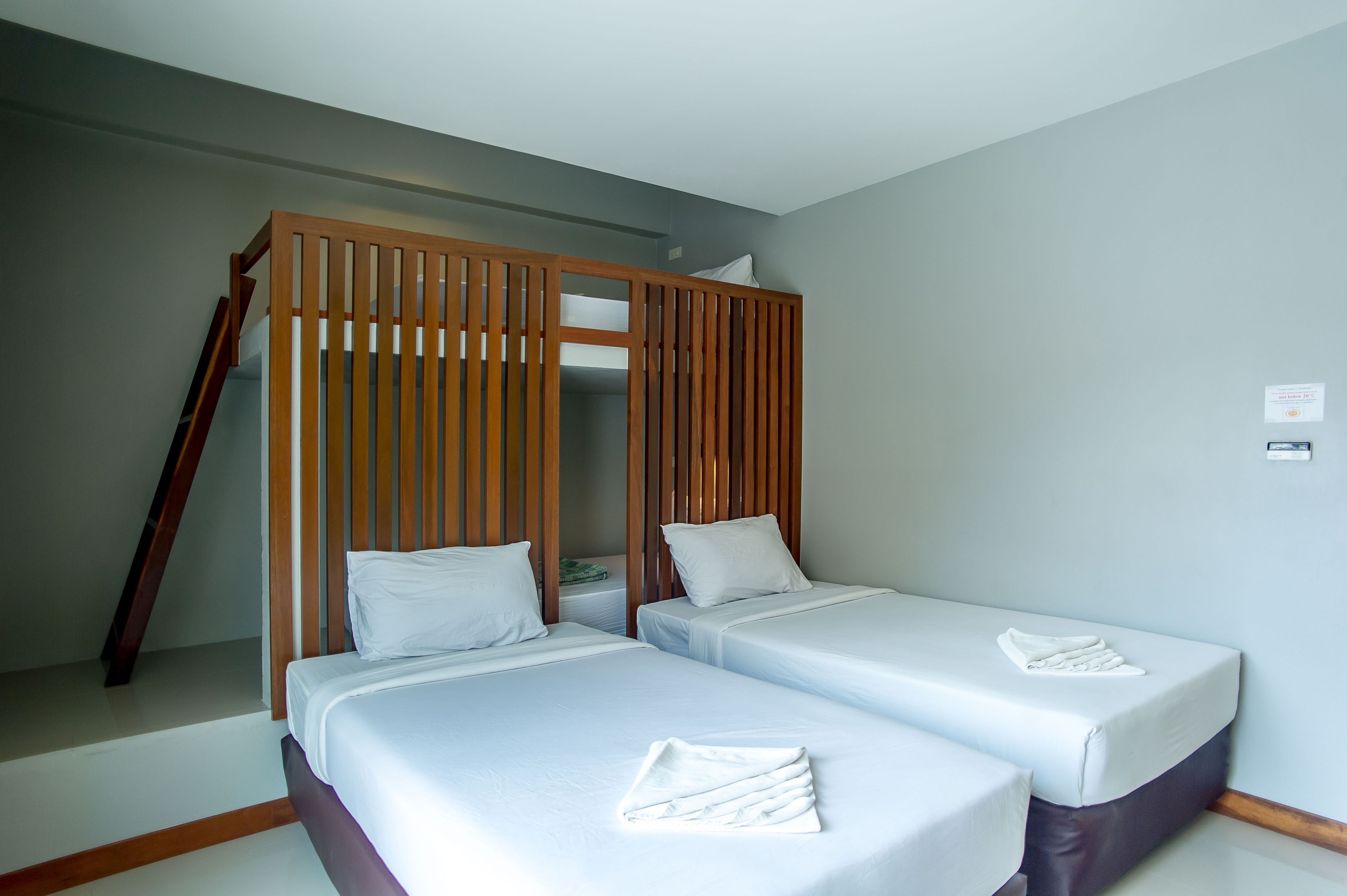 A hotel room with two single beds, a wooden partition, and a small table with a pillow.