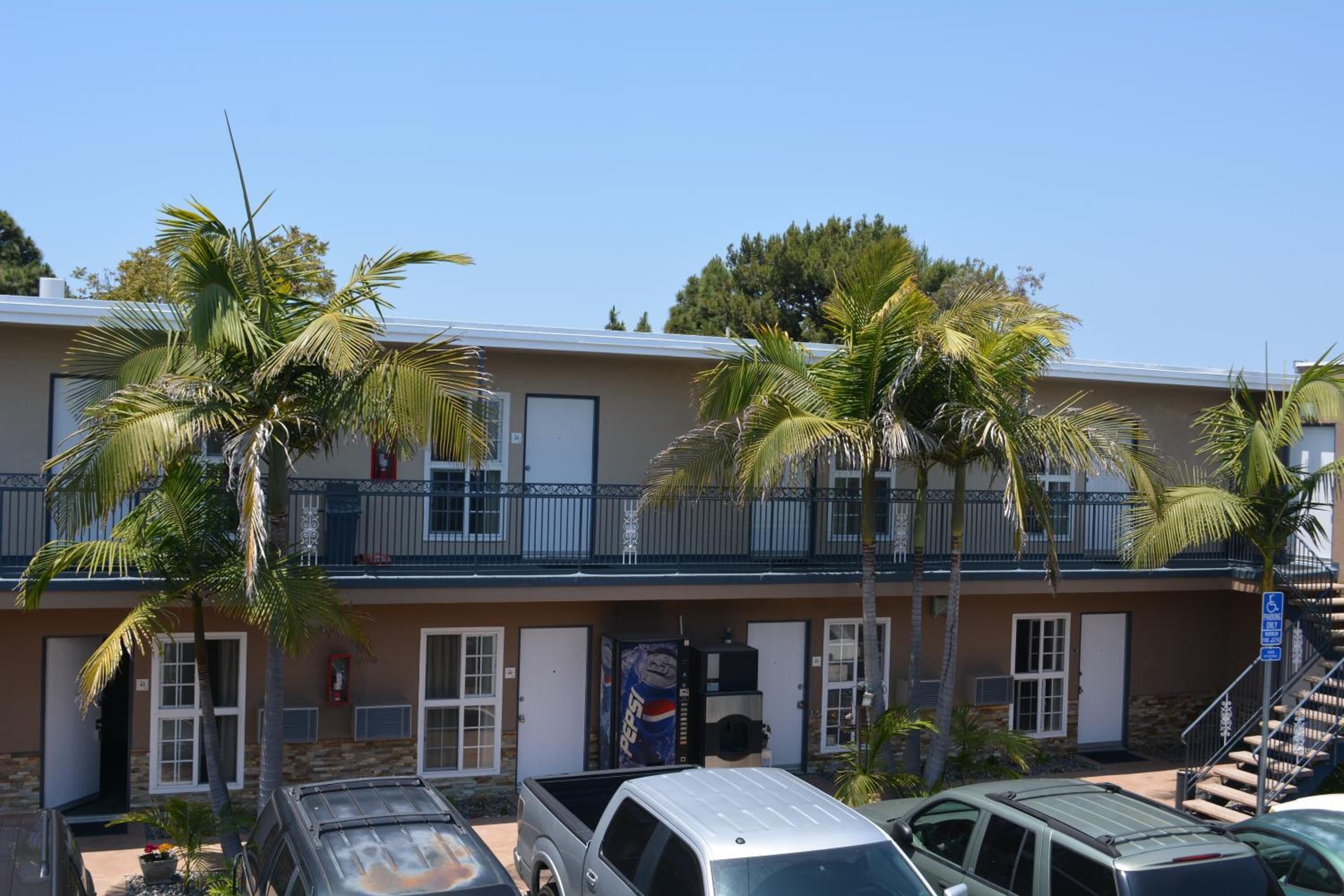 A motel with a two-story structure, a parking area, and palm trees.