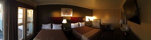Una habitación de hotel con dos camas, un escritorio, una silla, un televisor y una ventana con cortinas.