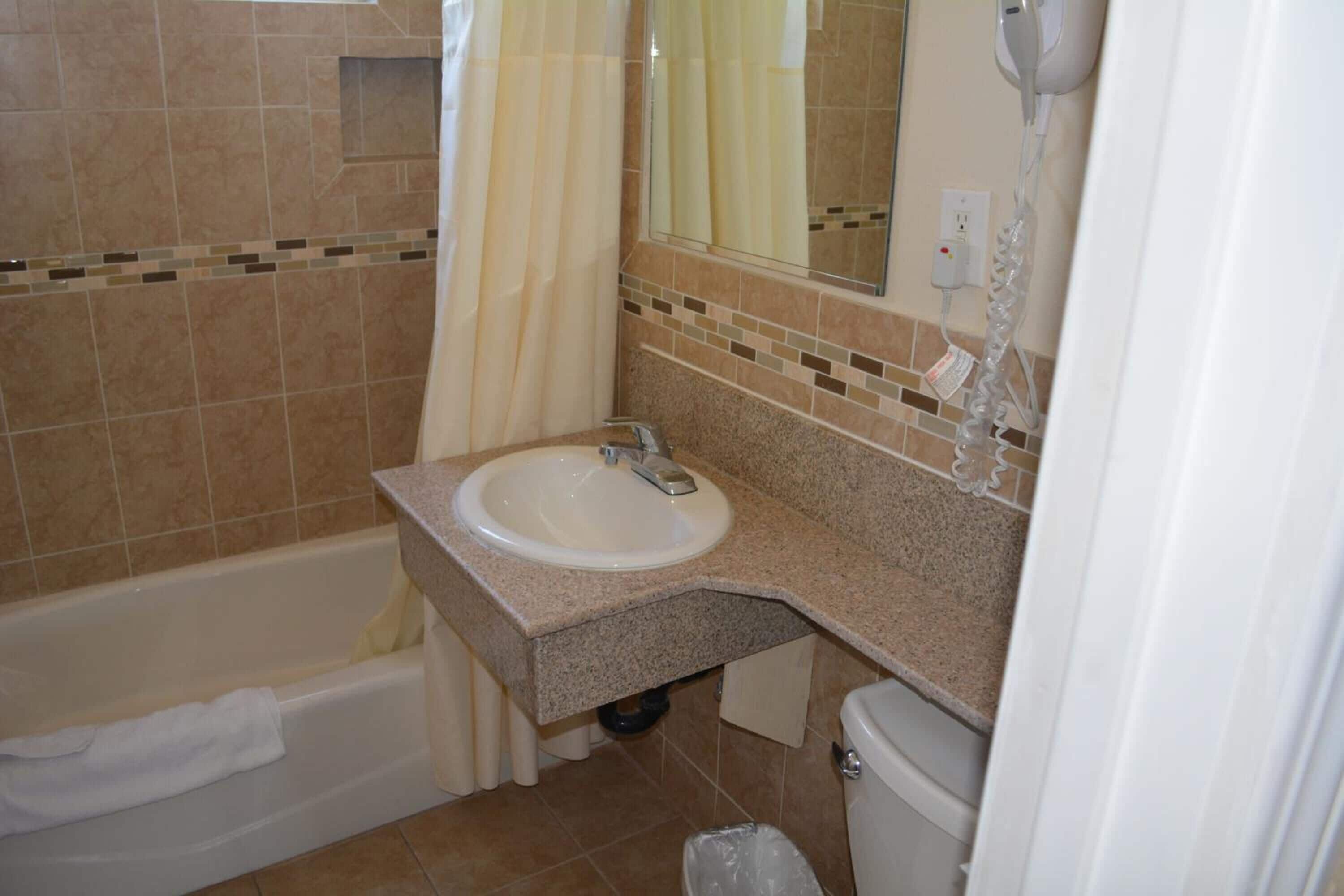 Un baño con lavamanos, espejo, cortina de ducha y un secador de pelo en la pared.