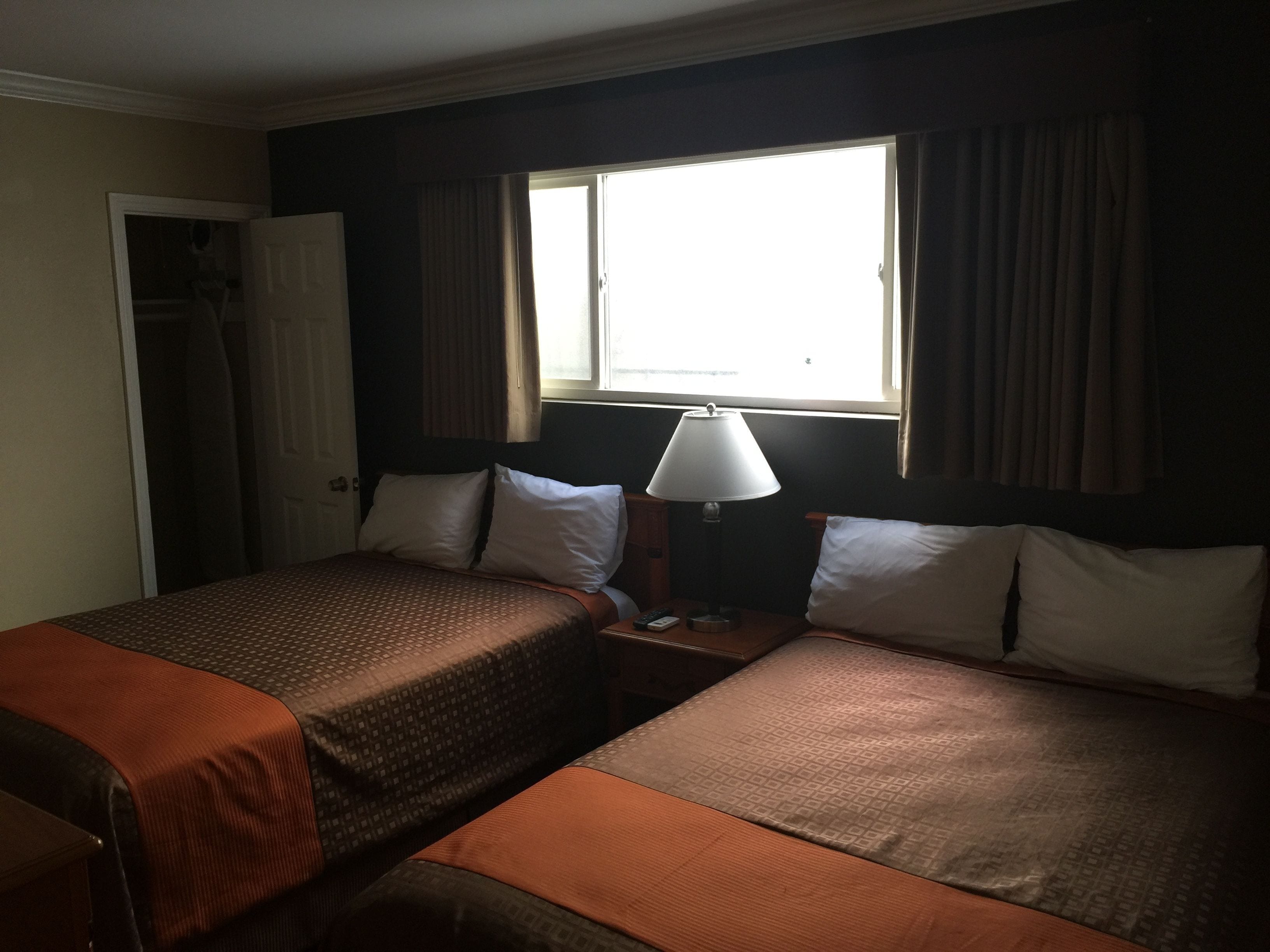 Une chambre d’hôtel avec deux lits, une table de chevet, une lampe et une fenêtre avec des rideaux.