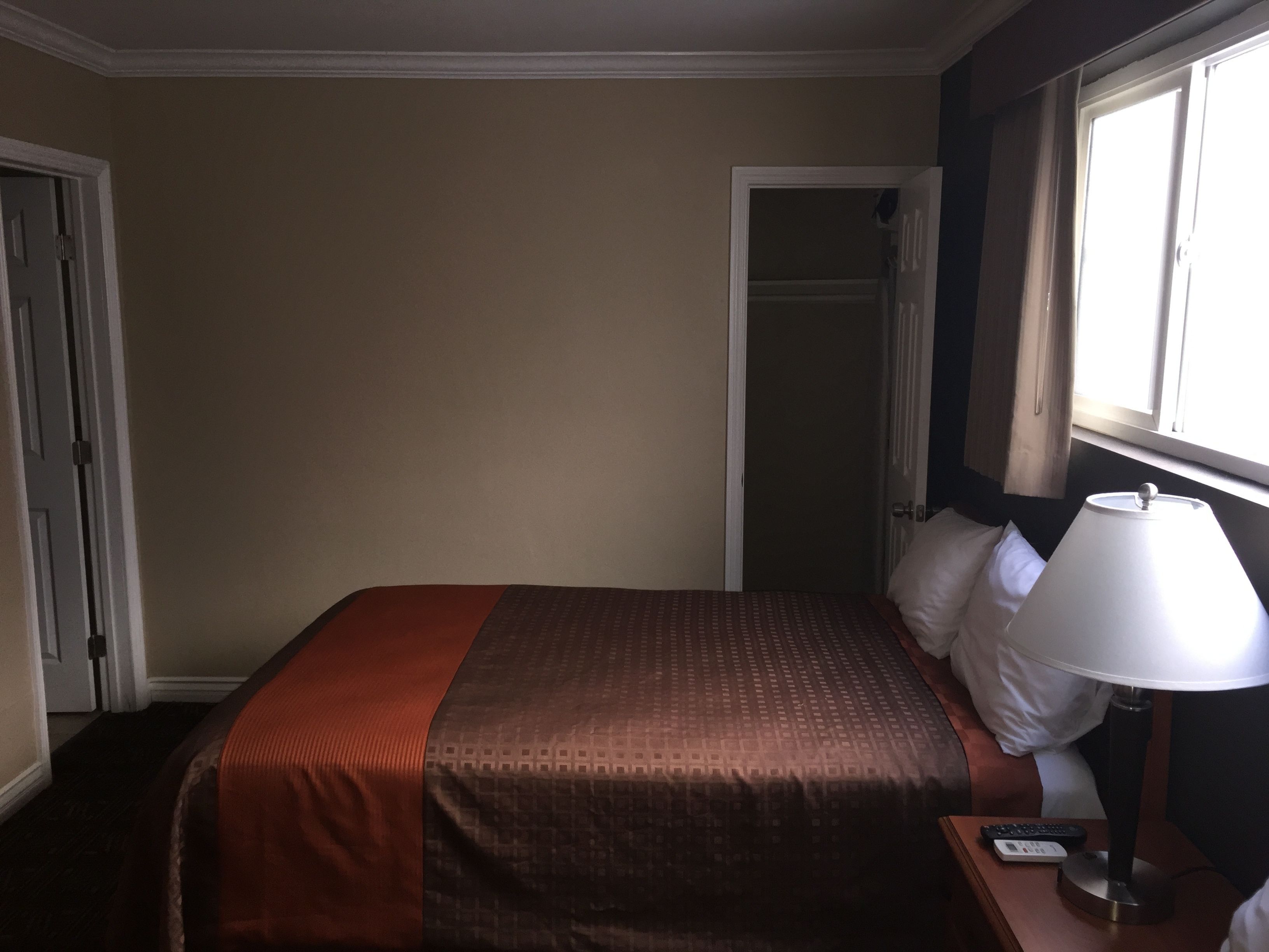 Habitación de hotel con cama, mesita de noche, lámpara y ventana.