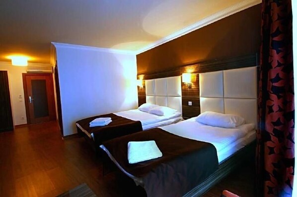 A hotel room with two single beds, a wooden floor, and a large window with curtains.