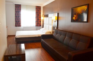 A hotel room with a bed, a sofa, a small table, and a painting on the wall.