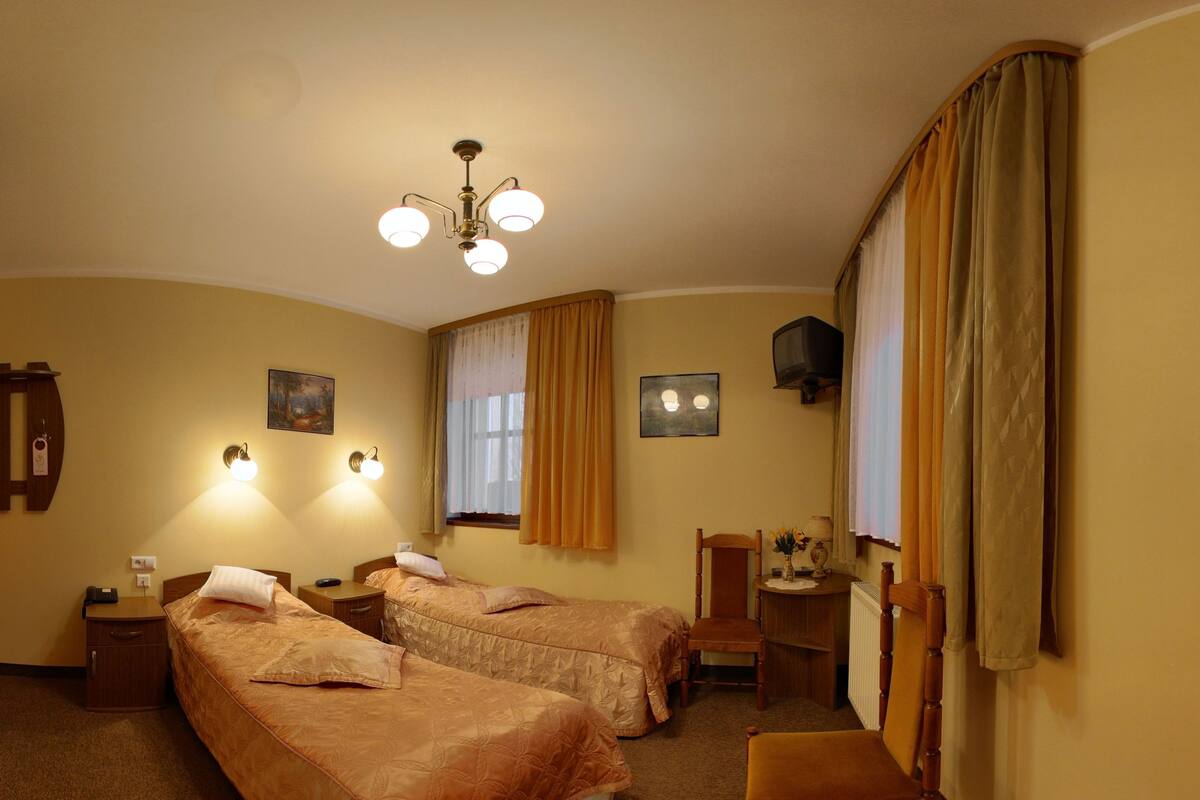 Ein Hotelzimmer mit zwei Betten, einem Schreibtisch, einem Sessel, einem Fernseher und einem Deckenventilator.