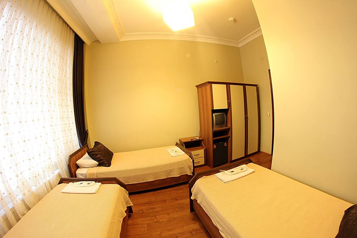 A hotel room with two single beds, a wooden wardrobe, a television, and a mirror.
