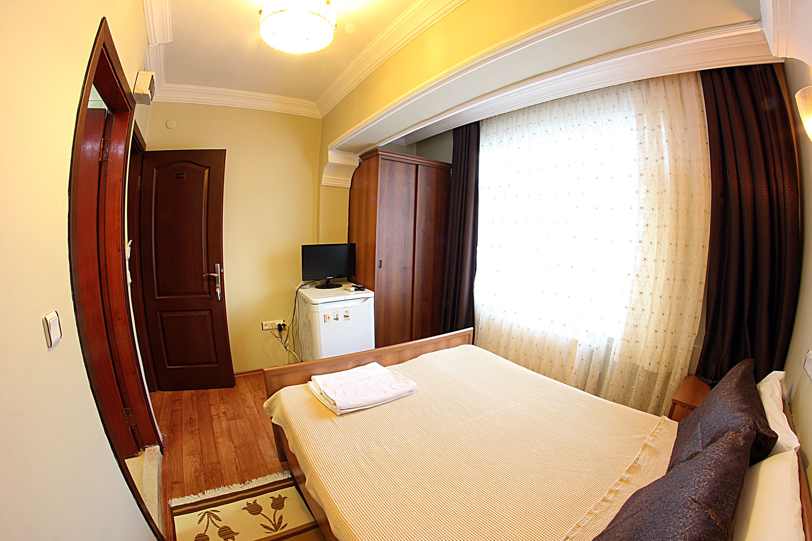 A hotel room with a bed, a wardrobe, a desk with a computer, and a window with curtains.