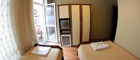 Habitación de hotel con dos camas, un armario, televisor y puerta corrediza de vidrio que da a un balcón.