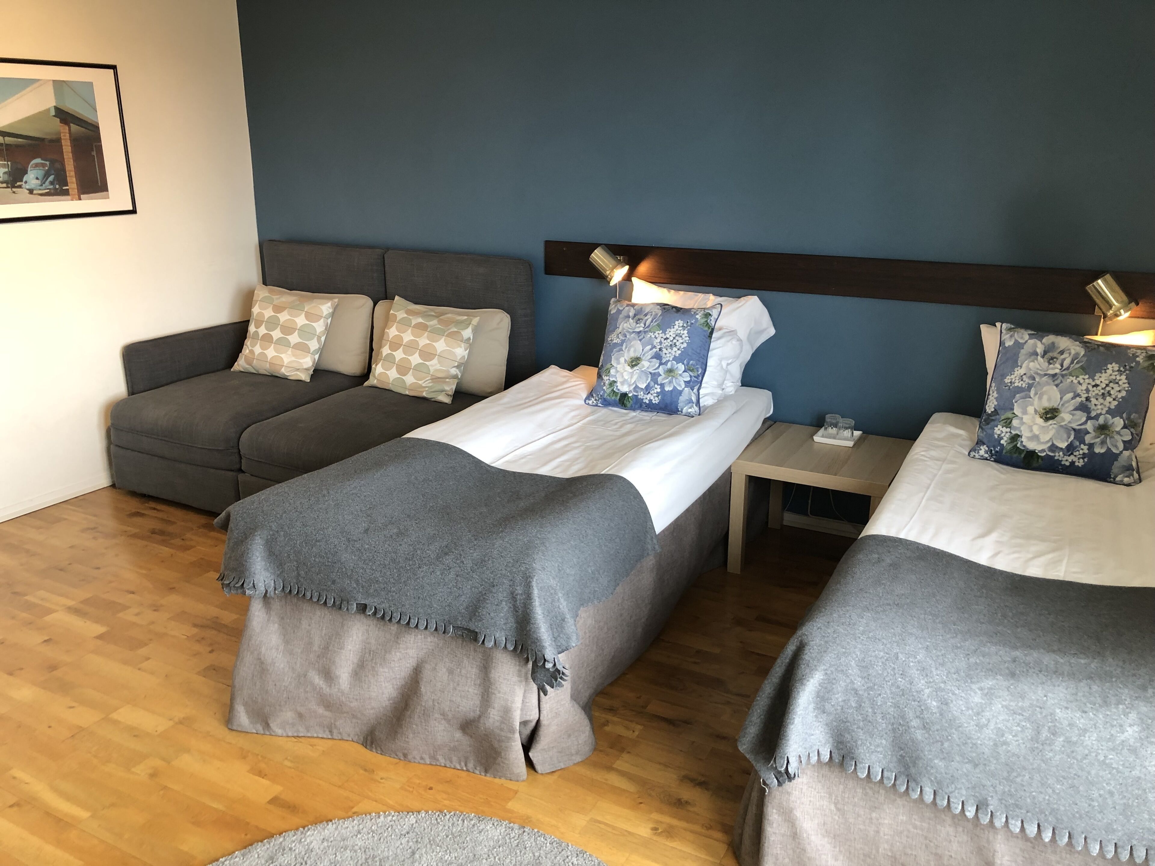 A hotel room with two single beds, a sofa, a small table, and a wall-mounted lamp.