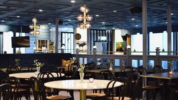 Ein Restaurant mit runden Tischen und schwarzen Stühlen, mit modernem Deckenstil und großen Fenstern.