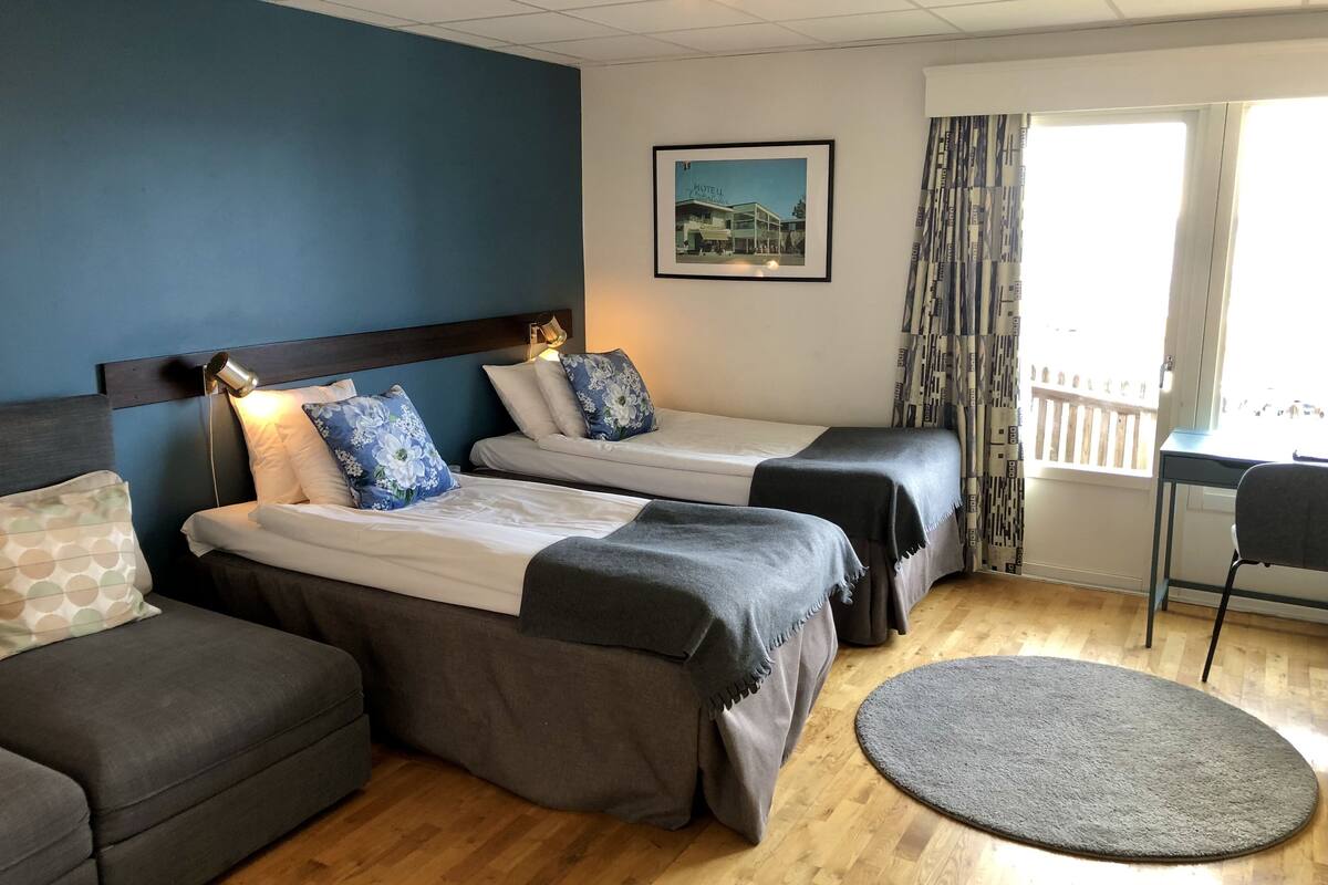 A hotel room with two beds, a sofa, a desk, and a window with curtains.