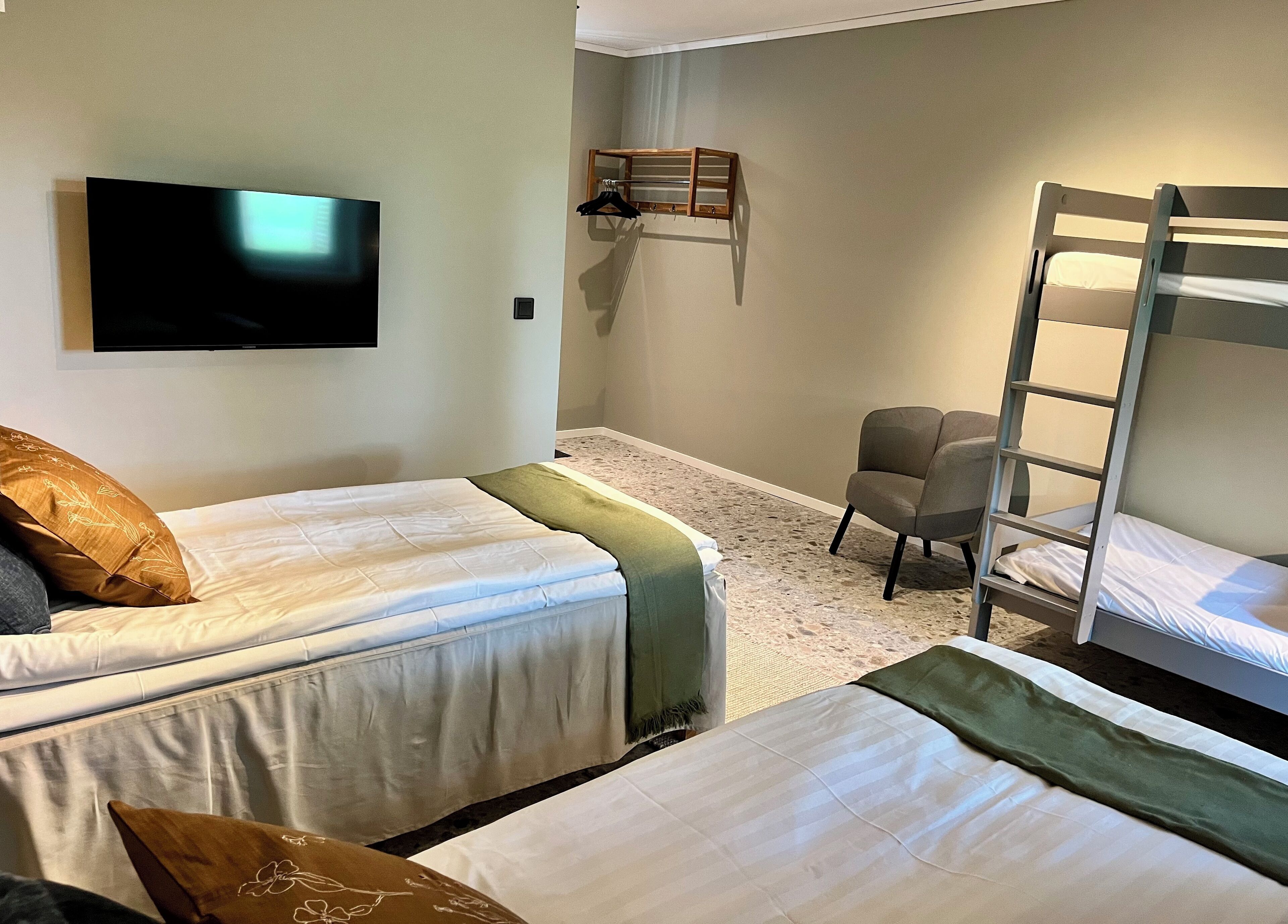 Un dormitorio con dos camas individuales, una litera y una televisión montada en la pared, además de una silla.