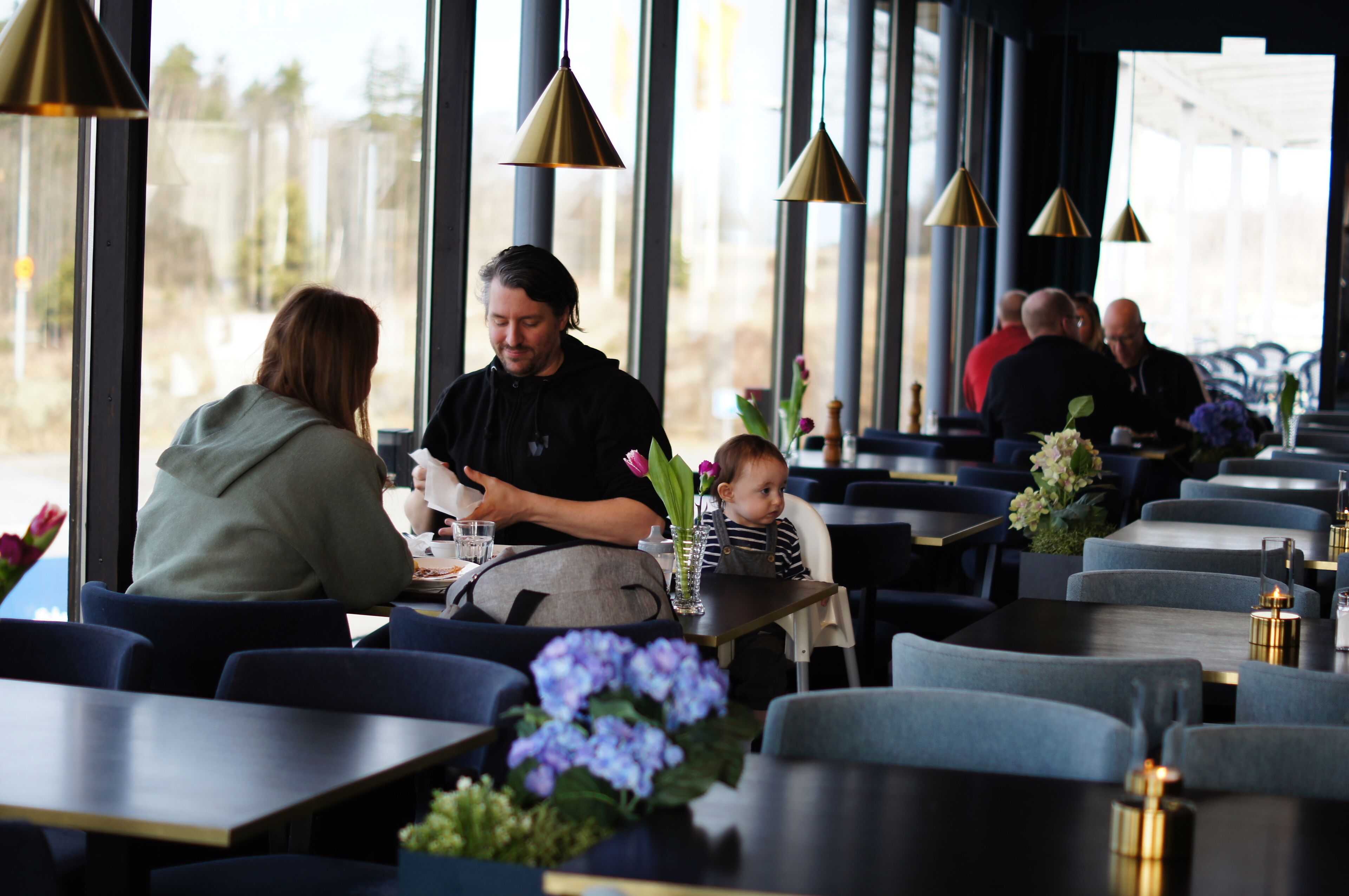 A restaurant with a modern interior, featuring rows of tables and chairs, large windows, and pendant lighting.